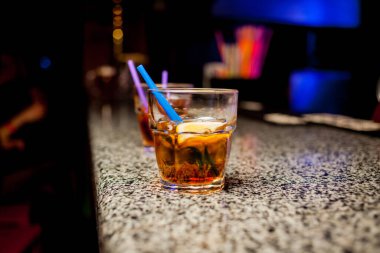 Bar arka planında bir bardak buzlu kokteyl. Siyah arka planda Bokeh ışığı olan camlı bir Wiskey. Bir bardak viski. Barın arka planında bir bardak viski ve buz..