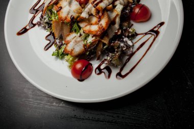 Kalamarlı salata, marul, lahana, vişneli domates ve sos. Kalamar dilimli salata, beyaz tabakta, siyah arka planda. Yakın plan fotoğraf, yumuşak odaklanma. Yemek tarifi kitabı için fotoğraf, restoran menüsü