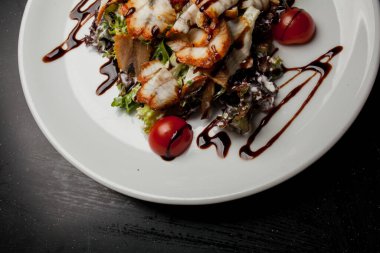 Kalamarlı salata, marul, lahana, vişneli domates ve sos. Kalamar dilimli salata, beyaz tabakta, siyah arka planda. Yakın plan fotoğraf, yumuşak odaklanma. Yemek tarifi kitabı için fotoğraf, restoran menüsü