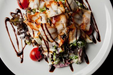 Kalamarlı salata, marul, lahana, vişneli domates ve sos. Kalamar dilimli salata, beyaz tabakta, siyah arka planda. Yakın plan fotoğraf, yumuşak odaklanma. Yemek tarifi kitabı için fotoğraf, restoran menüsü