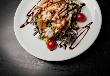 Kalamarlı salata, marul, lahana, vişneli domates ve sos. Kalamar dilimli salata, beyaz tabakta, siyah arka planda. Yakın plan fotoğraf, yumuşak odaklanma. Yemek tarifi kitabı için fotoğraf, restoran menüsü