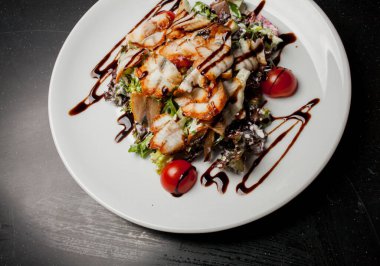 Kalamarlı salata, marul, lahana, vişneli domates ve sos. Kalamar dilimli salata, beyaz tabakta, siyah arka planda. Yakın plan fotoğraf, yumuşak odaklanma. Yemek tarifi kitabı için fotoğraf, restoran menüsü