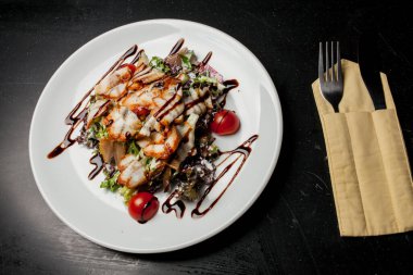 Kalamarlı salata, marul, lahana, vişneli domates ve sos. Kalamar dilimli salata, beyaz tabakta, siyah arka planda. Yakın plan fotoğraf, yumuşak odaklanma. Yemek tarifi kitabı için fotoğraf, restoran menüsü