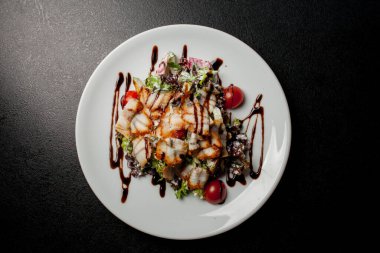 Kalamarlı salata, marul, lahana, vişneli domates ve sos. Kalamar dilimli salata, beyaz tabakta, siyah arka planda. Yakın plan fotoğraf, yumuşak odaklanma. Yemek tarifi kitabı için fotoğraf, restoran menüsü