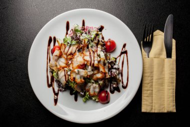 Kalamarlı salata, marul, lahana, vişneli domates ve sos. Kalamar dilimli salata, beyaz tabakta, siyah arka planda. Yakın plan fotoğraf, yumuşak odaklanma. Yemek tarifi kitabı için fotoğraf, restoran menüsü