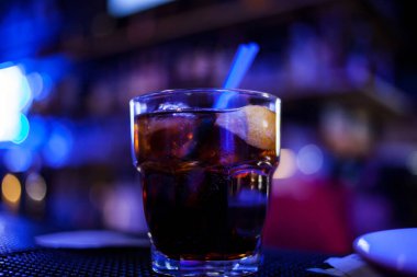 Bar arka planında bir bardak buzlu kokteyl. Siyah arka planda Bokeh ışığı olan camlı bir Wiskey. Bir bardak viski ve kola. Barın arka planında bir bardak viski ve buz. neon ışığı
