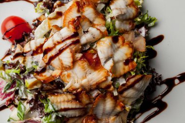 Kalamarlı salata, marul, lahana, vişneli domates ve sos. Kalamar dilimli salata, beyaz tabakta, siyah arka planda. Yakın plan fotoğraf, yumuşak odaklanma. Yemek tarifi kitabı için fotoğraf, restoran menüsü