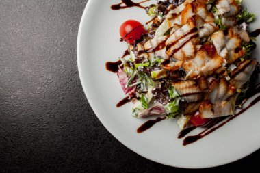 Kalamarlı salata, marul, lahana, vişneli domates ve sos. Kalamar dilimli salata, beyaz tabakta, siyah arka planda. Yakın plan fotoğraf, yumuşak odaklanma. Yemek tarifi kitabı için fotoğraf, restoran menüsü