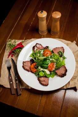 Yeşillikli et biftekleri, kayısılar ve büyük beyaz bir tabak üzerine sos. Yemek arkaplanı için bambu hasırı. Çatal bıçak takımı, ahşap biber ve tuzluk var. Barbekü, barbekü.