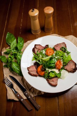 Yeşillikli et biftekleri, kayısılar ve büyük beyaz bir tabak üzerine sos. Yemek arkaplanı için bambu hasırı. Çatal bıçak takımı, ahşap biber ve tuzluk var. Barbekü, barbekü.