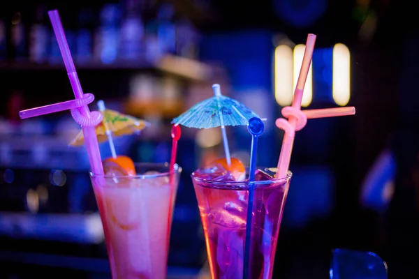 Fresh tall glass of tropical cocktail with juice at bar counter background.Cocktail glasses with ice and holiday lights in the background.Margarita cocktail in a glass on a background of bright lights