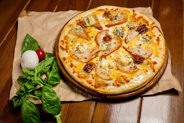 Armutlu pizza, ceviz, Dorbl peyniri ve limon yağı. Kahverengi ahşap bir masa üzerinde armut, ceviz ve gorgonzola ile ev yapımı pizza. El yapımı kağıt. Pizzanın yanında mantar, kuş ve kirazlı domates var..