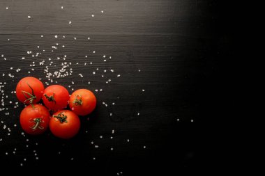 Siyah arka planda baharatlı taze kiraz domatesleri. Kopyalama alanı olan üst görünüm. Siyah ahşap zemin üzerinde taze kiraz domatesleri ve deniz tuzu..