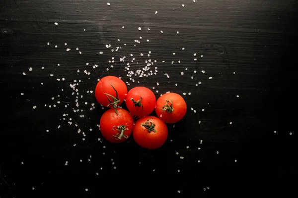 Fresh cherry tomatoes on a black background with spices. Top view with copy space. Fresh cherry tomatoes on a black wooden background with sea salt.