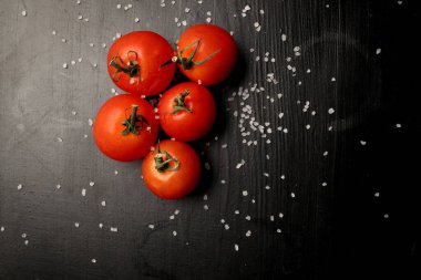 Siyah arka planda baharatlı taze kiraz domatesleri. Kopyalama alanı olan üst görünüm. Siyah ahşap zemin üzerinde taze kiraz domatesleri ve deniz tuzu..