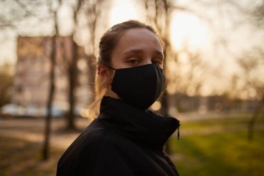 Siyah ceketli bir kız ve parkta siyah bir maske. Siyah tıbbi maskeli bir kız sokakta. Karantinaya alındı. Kendini soyutlama. Siyah tıbbi maskeli bir kızın portresi..