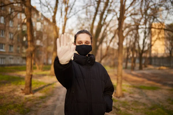 Siyah ceketli ve siyah maskeli bir kız elinde DUR işareti ile beliriyor. Siyah tıbbi maskeli bir kız sokakta. Karantinaya alındı. Kendini soyutlama. Siyah maskeli bir kızın portresi..