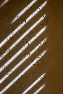 Shade from the blinds on the wall with plaster. Thin lines of light on the wall. The texture of the plaster. Shadow from the blinds. Place for your text.