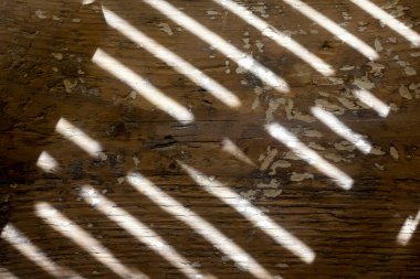 Shade from the blinds on the wall with plaster. Thin lines of light on the wall. The texture of the wood. Shadow from the blinds. Place for your text.