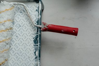 Roller with a red handle in a green pallet with white paint. Bucket with paint and a tray for paint and varnish. Roller and pallet with paint for rollers. Copy space for text. Concept of construction.