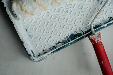 Roller with a red handle in a green pallet with white paint. Bucket with paint and a tray for paint and varnish. Roller and pallet with paint for rollers. Copy space for text. Concept of construction.