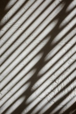 Shade from the blinds on the wall with plaster. Thin lines of light on the wall. The texture of the plaster. Shadow from the blinds. Place for your text.