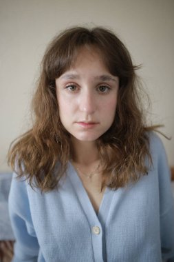 Mavi bluz giymiş üzgün, kahverengi saçlı, beyaz bir kadın. 