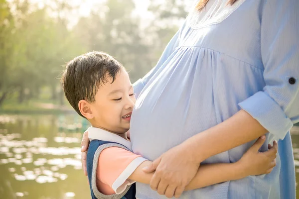 Asian boy kissing the belly of his pregnant mother — Stock Photo, Image