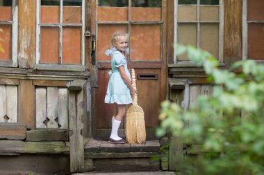 Süpürgeyle gezen bir kız, annesinin evin verandasını süpürmesine yardım eder. Çocuklar yardımcıdır. Evi temizliyorum. Çocuklar Rusya, SSCB