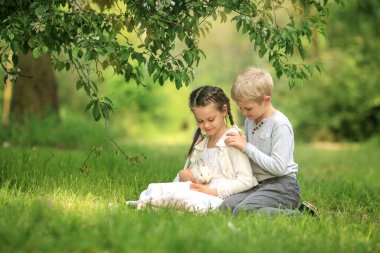 Bir kızla oynayan bir oğlan çiçek açan elma ağacının altında oturuyor.