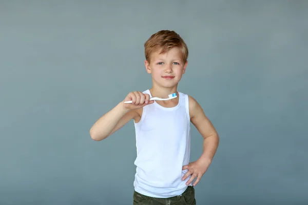 Cute smiling boy in a white T-shirt holding a toothbrush in hands. The concept of children and medicine