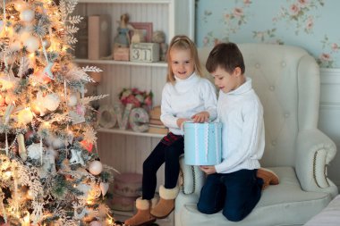 Güzel küçük kız 3 yaşında sarışın oğlan ve 5 yaşında Noel ağacının altında hediyelerin yanında oturuyor.