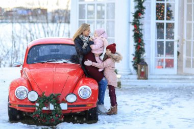 Anne ve kızı, kırmızı bir araba ve uçan bir karla kış parkında yürüyor.