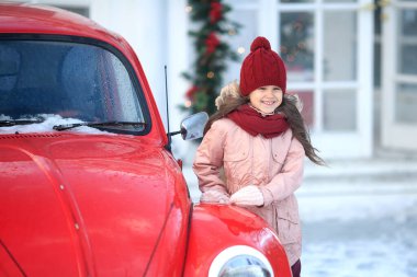 Karlı bir günde kış yürüyüşünde şapkalı ve eşarplı deochka Noel ağacının yanında kırmızı avtomozhilya ve parlayan gerlyandami 'nin yanında duruyor. Yeni Yıl