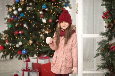 Sıcak pembe ceketli, şapkalı bir kız Noel ağacının avlusunda el ele tutuşmuş, ateş püskürüyor, kar yağıyor.