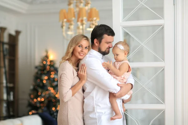 beautiful blond family mother, father and daughter are beard behind the house is decorated with Christmas tree