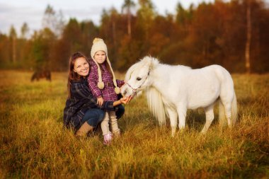 Sonbahar parkında kazaklı, kot pantolonlu ve spor ayakkabılı iki kardeş balkabağının yanında bir sepetin üzerinde oturuyorlar ve ellerinde sarı yapraklardan oluşan bir elma ve sonbahar buketi tutuyorlar.