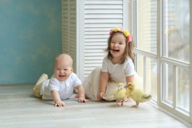 Sarı elbiseli kız ve oğlan genç kazlarla oynuyorlar.