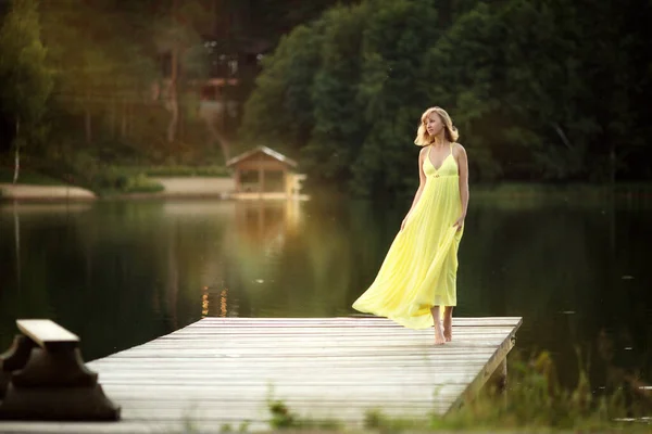 Блондинка Жёлтом Платье Идёт Деревянному Мосту Возле Реки — стоковое фото