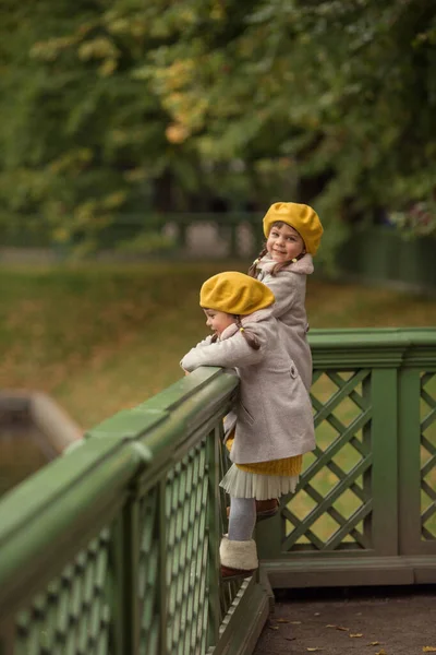 コートを着た姉妹の双子と黄色のベレー帽はサンクトペテルブルクで歩いています サンクトペテルブルク 夏の庭への旅行 — ストック写真