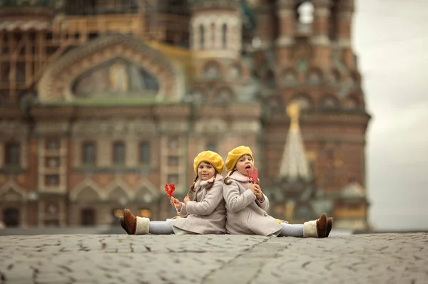 身穿外套和黄色贝雷帽的孪生姐妹坐在血泊中 吃着糖果 圣彼得堡的步行儿童 — 图库照片