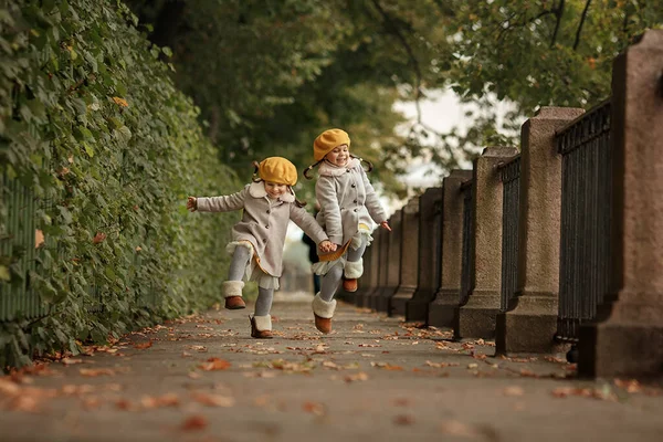 二人の女の子の双子が手をつないで走る 秋の公園でゲーム 幼少期 姉妹期 — ストック写真