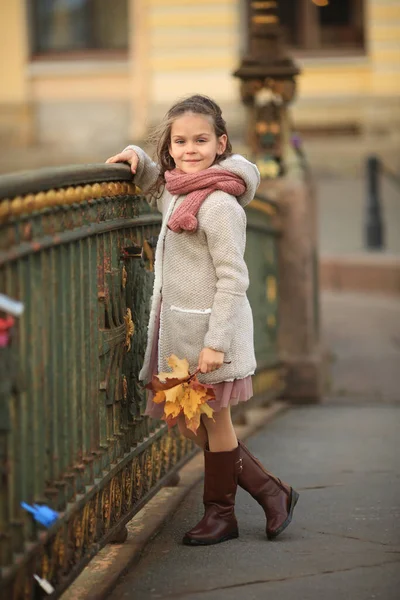 秋のコートを着た長髪の女の子と サンクトペテルブルクの橋の上に立つスカーフは 秋のメープルの花束を手にしています 髪に風 — ストック写真