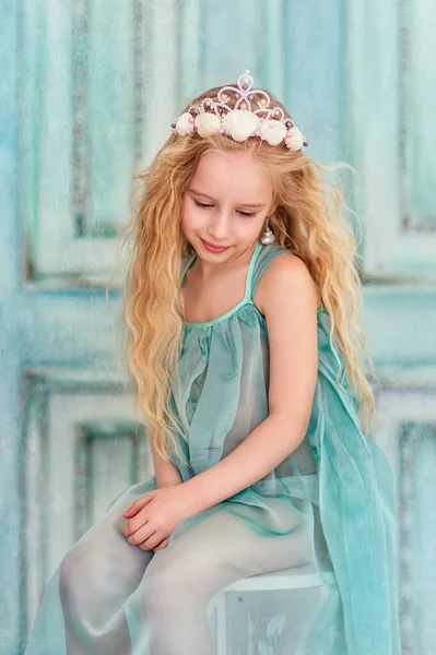 青いドレスの椅子に座って貝殻の冠を持つ長いブロンドの髪の美しい小さな女の子 子供と海の概念 青の背景 — ストック写真