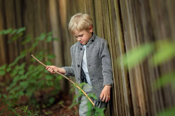 いじめっ子少年は木の棒で柵のそばに立って — ストック写真