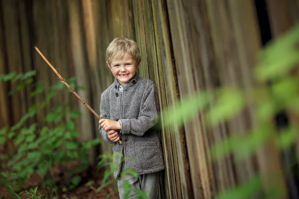 木製の棒を持った柵のそばに立って笑っている少年 — ストック写真
