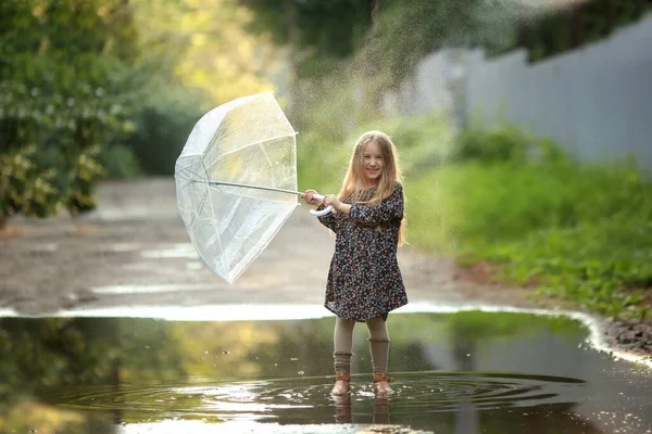 머리에 우산을 아름다운 드레스와 신발을 소녀는 빗속의 흙탕물 달린다 — 스톡 사진