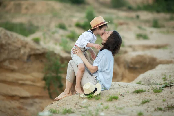 優しいお母さんは息子と一緒に湖の砂の上に座って抱き合って夏の日にキスをして遊んでいます — ストック写真