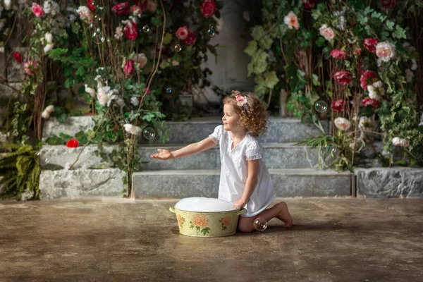 白いドレスの女の子と骨盤のカールの打撲は夏の庭でシャボン玉で遊んでいます — ストック写真