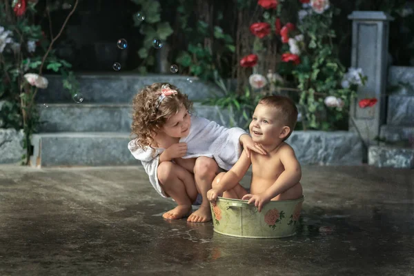家の中庭の骨盤に座っている弟を洗うタオルに包まれた中赤ちゃん — ストック写真